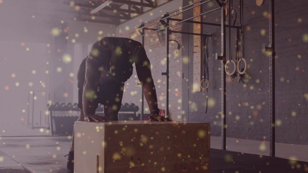 Mand placerer hænder på en fitness plyo-boks, skifter vægt og hviler, mens gyldne partikler svæver.