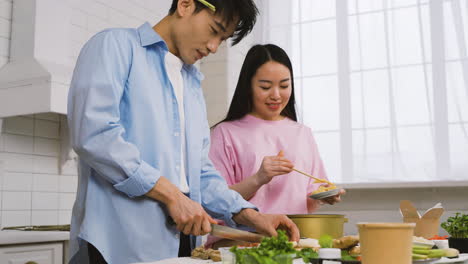 pareja japonesa cocinando comida japonesa mientras habla y se ríe en la cocina