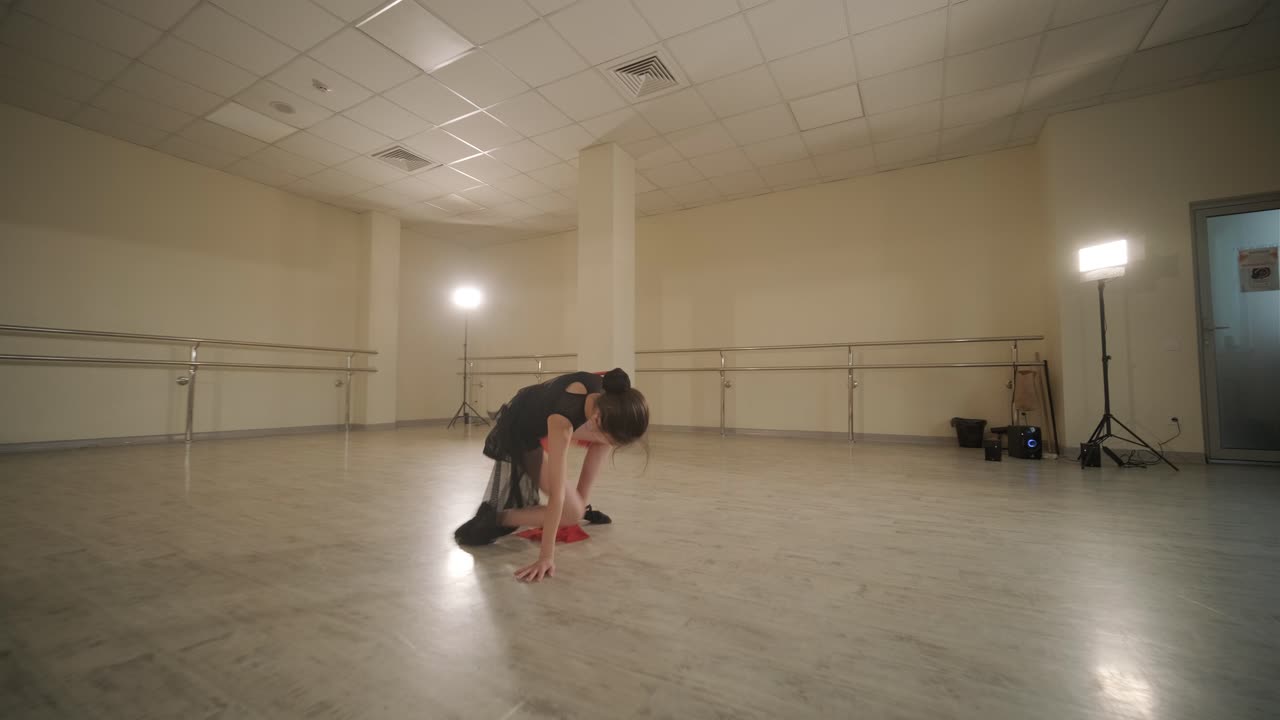 Un gruppo di giovani allievi di danza classica in abbigliamento da ballo nero che eseguono esercizi in un ampio studio di danza con pavimenti in legno e barre a muro. Espressioni concentrate e movimenti sincronizzati