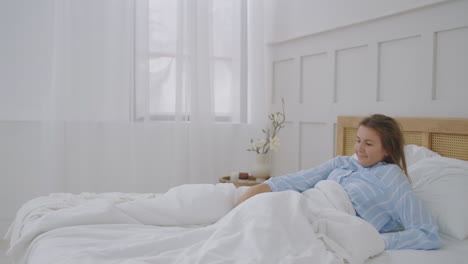 hermosa morena despertando lentamente por la mañana se estira y se levanta de la cama el sol brilla sobre ella desde la gran ventana. feliz joven saluda el nuevo día