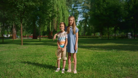 Cute-smiling-sister-hugging-brother.-Kids-pose-on-green-lush-field-with-rackets