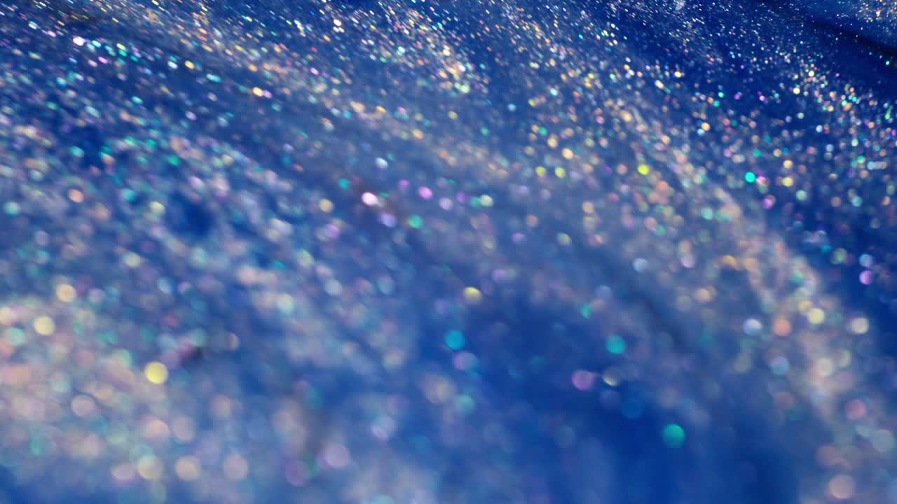 A close-up view of shimmering blue glitter with rainbow reflections, suggesting ink mixing