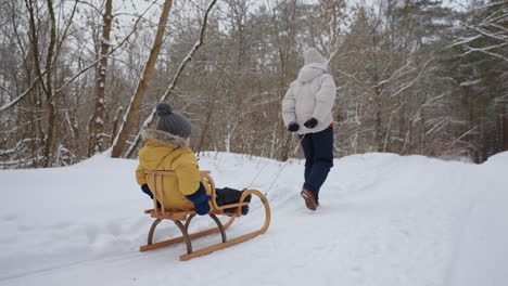 Frau-Zieht-Holzschlitten-Mit-Kleinem-Kind-Darin-Und-Geht-Im-Winter-Im-Wald-Spazieren