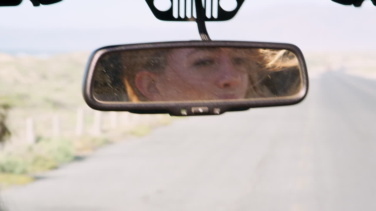 Young woman's face reflected in mirror of driving car