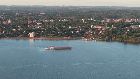 drone view of commercial vessel navigating near coastal city, export and import trade