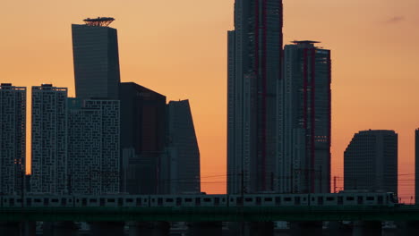 Die-U-Bahn-Von-Seoul-Fährt-über-Den-Han-Fluss-Auf-Der-Hangang-Eisenbahnbrücke-Mit-Blick-Auf-Die-Städtische-Skyline.-Yeouido-Wolkenkratzer,-Bürogebäude-Und-Geschäftsgebäude-Bei-Sonnenuntergang-–-Südkorea-Transport