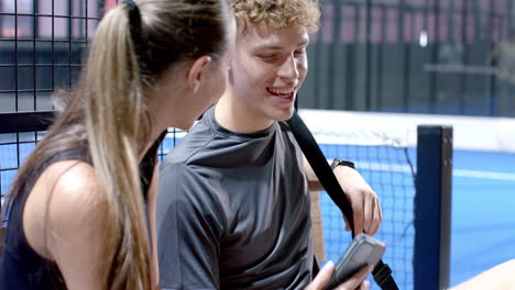 young woman discussing strategy with teammate on padel tennis on indoor court bench