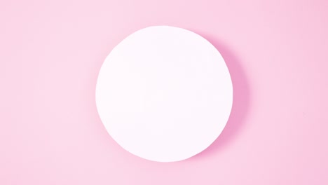 Vibrant Easter eggs appear under round paper card note on pastel pink background. Stop motion flat lay