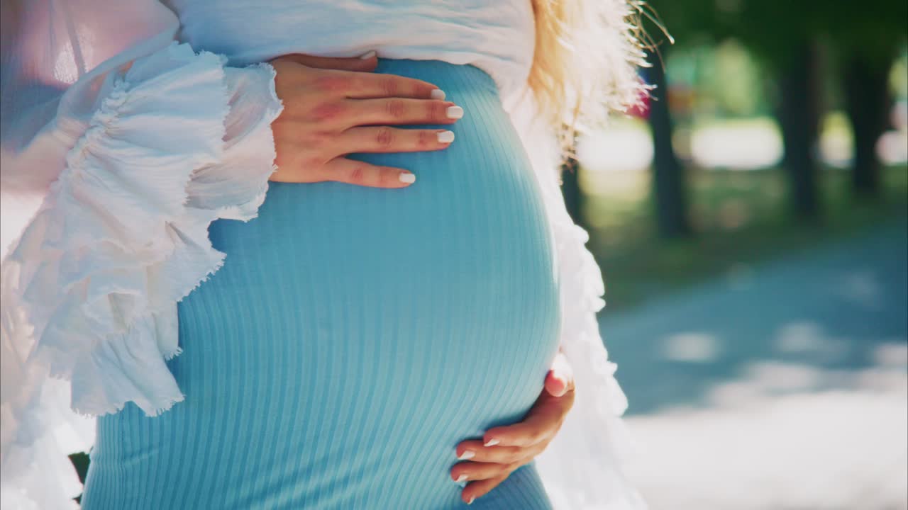Gravid kvinne som forsiktig kjærtegner babymagen sin utendørs