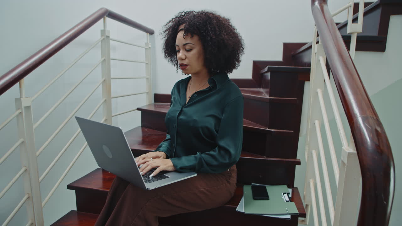 Curly Businesswoman Doing Report on Laptop Sitting on Steps in Home Office