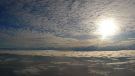 aerial still shot from plane window: sun behind clouds, blue sky, late-day shadows