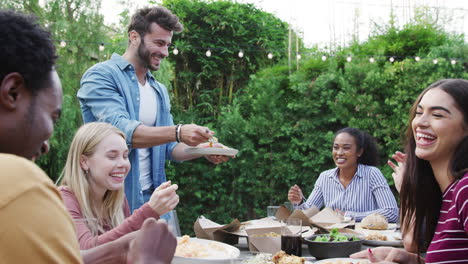 Amigos-Multiculturales-En-Casa-Sentados-A-La-Mesa-Disfrutando-De-La-Comida-En-La-Fiesta-De-Verano-En-El-Jardín