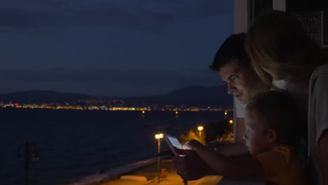 parents and child with pad on hotel balcony at night