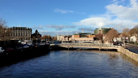 A-low-drone-shot-of-Rowers-on-the-River-Liffey-passing-under-the-Frank-Sherwin-Bridge-in-Dublin-Ireland-upstream-towards-Heuston-train-Station-on-a-sunny-calm-Saturday-evening