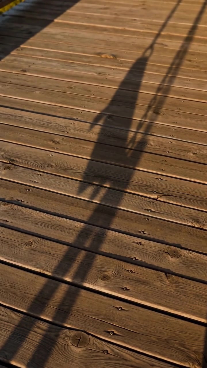 Time-sequence showing person silhouette progressing across outdoor wooden deck from early to near-end frames, warm low-angle sunlight from left casts long