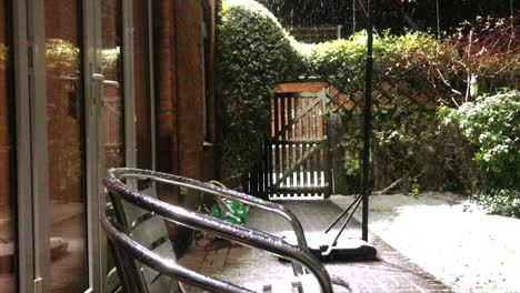 Snow-falling-on-stacked-metal-chairs-in-backgarden-in-front-of-a-wooden-gate