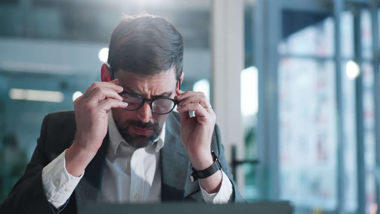 Focused Businessman Puts on Glasses While Working on Laptop in Office