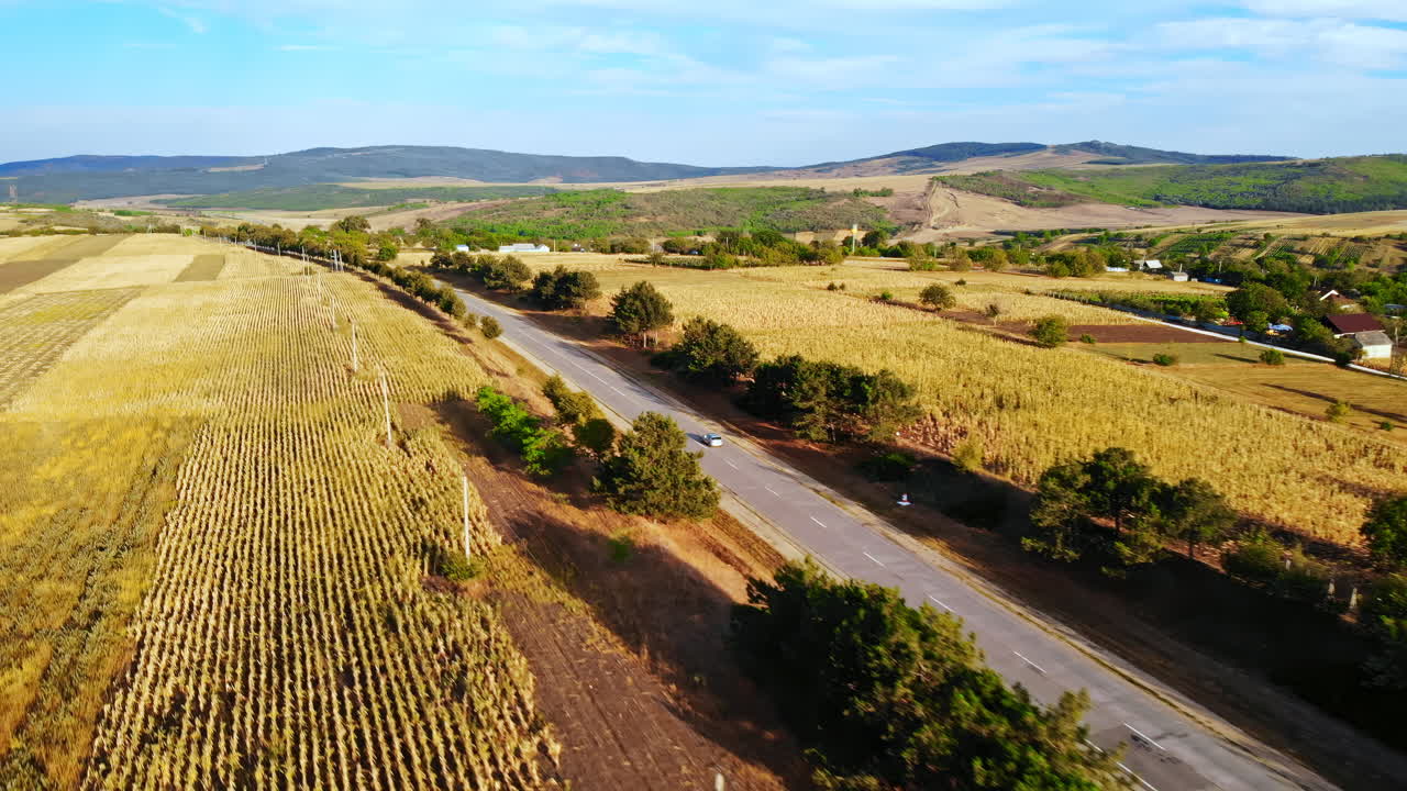 Aerial drone view of a road with moving car in highland. Small village and green hills on background. Sunny day. Balti, Moldova