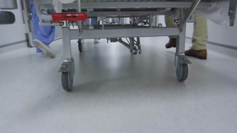 feet of doctors walking through corridor transporting patient in bed on wheels