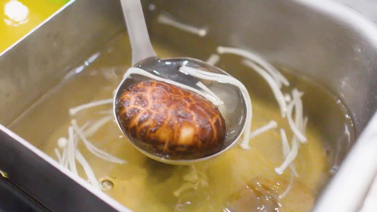 Close-up shot of a ladle lifting mushrooms from simmering broth in a divided restaurant pot