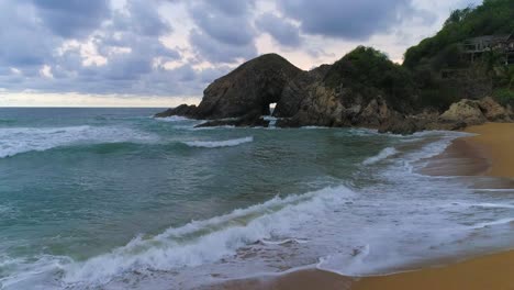 Dolly-En-Tiro-Sobre-Rocas-En-Playa-Zipolite-Con-Una-Gran-Formación-Rocosa,-Oaxaca