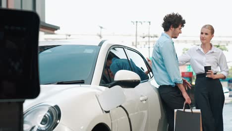 hombre de negocios y mujer de negocios progresistas apoyándose en el coche y el punto de carga.