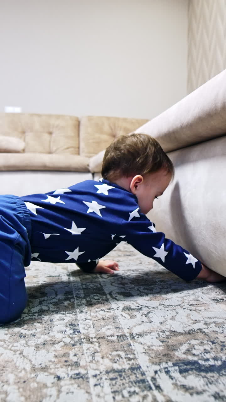 Baby boy trying to get under the sofa. Kid lies on the floor looking under the furniture. Child stands up and goes to his toys. Vertical video