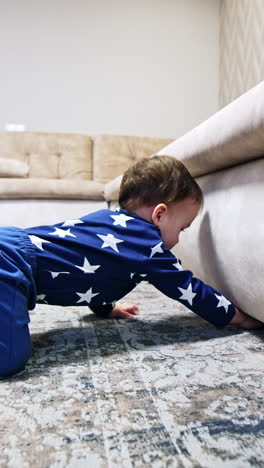 baby boy trying to get under the sofa. kid lies on the floor looking under the furniture. child stands up and goes to his toys. vertical video