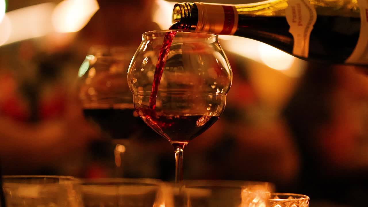 A bottle of red wine is poured into a glass in a warm, intimate setting with soft lighting