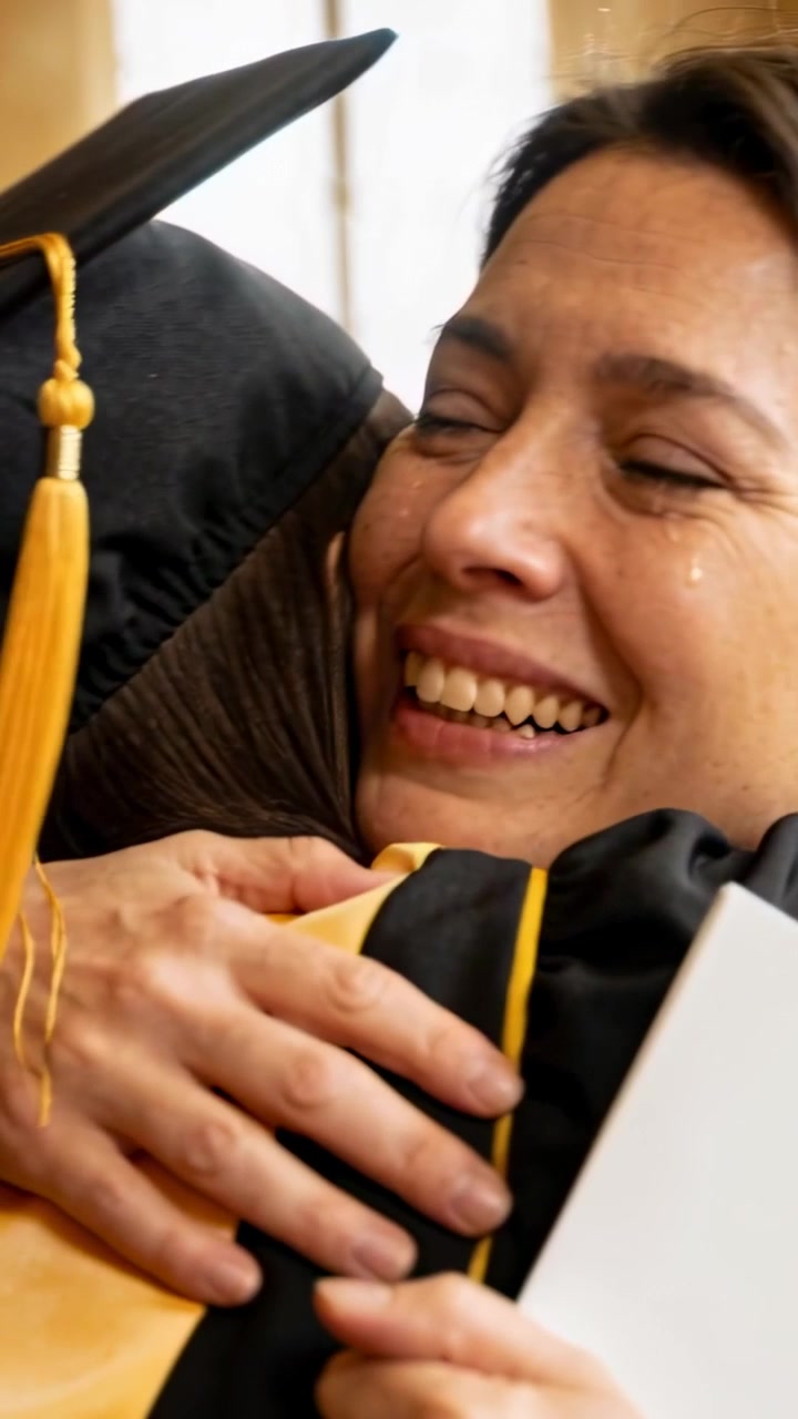 Video verticale: Durante la consegna del diploma, la mamma abbraccia il neolaureato con tocco e toga, che tiene in mano il diploma, festeggiando.