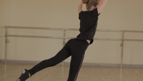 un grupo de jóvenes estudiantes de ballet con ropa de baile negra practicando posiciones en un amplio estudio de ballet con pisos de madera y barras montadas en la pared. expresiones enfocadas y movimientos sincronizados.