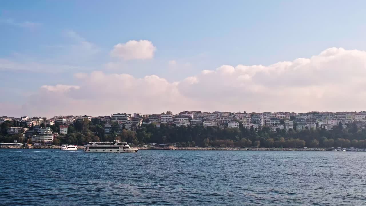A scenic seascape of Istanbul's historic Sarayburnu point. A ferry crosses the water with the ancient walls of Topkapi Palace and lush trees in the background