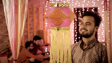 a smiling handsome man hanging a diwali traditional lantern during the festival.