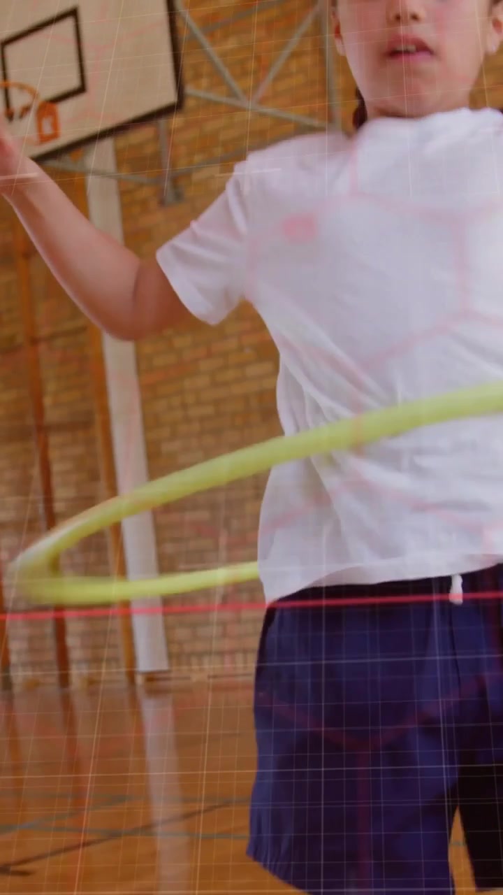 Vertical video: Girl shifting weight and rotating yellow hula hoop on gym court with red line in PE