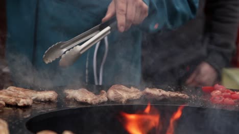 Kochen-Von-Fleisch,-Gemüse,-Feuer,-Grill,-Zeitlupe,-Pfannenrühren,-Koch-Mit-Küchenzange-In-Flammen-Und-Rauch,-Zubereitung-Einer-Köstlichen-Gourmet-Schweinefleisch-Hühnermahlzeit,-Camping-Im-Freien,-Nahaufnahme