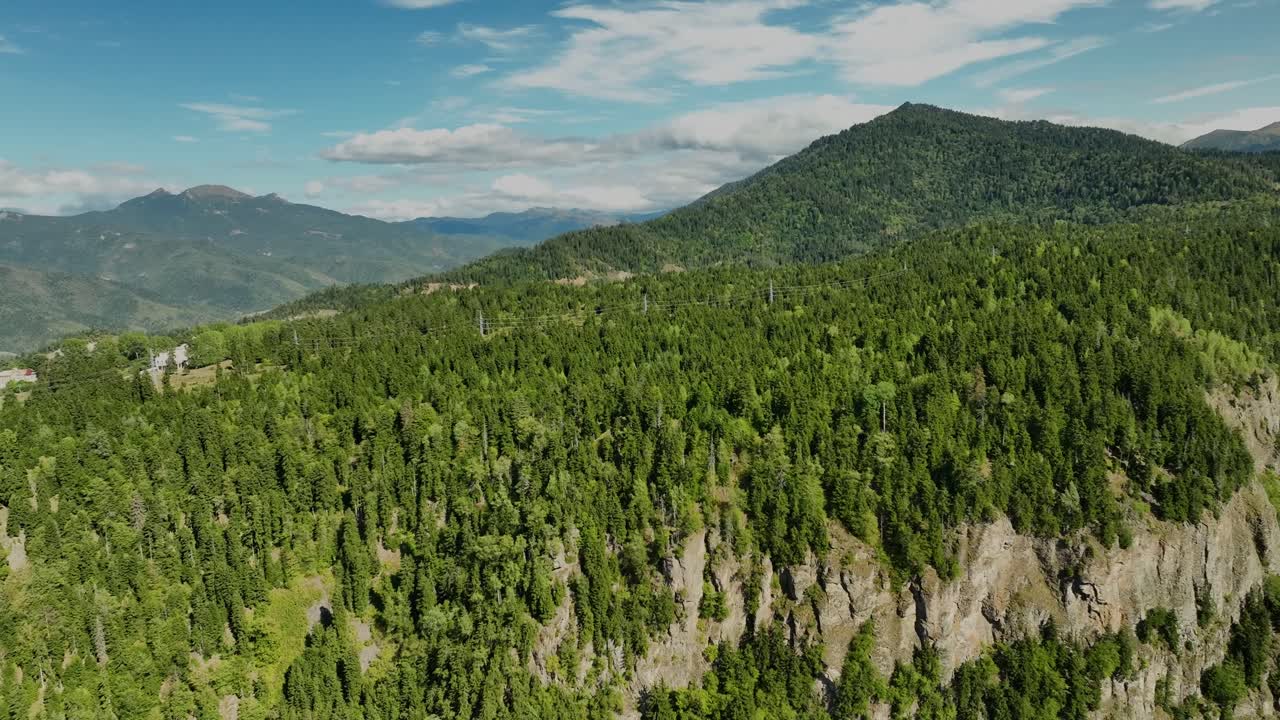 A breathtaking aerial image showing forested cliffs and green slopes in the Georgian highlands under bright summer skies