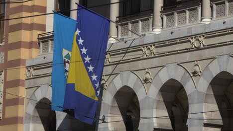 bosnia and herzegovina flag blowing in the wind after camera tilt up from bus and pedestrians on street. seen in sarajevo capital.