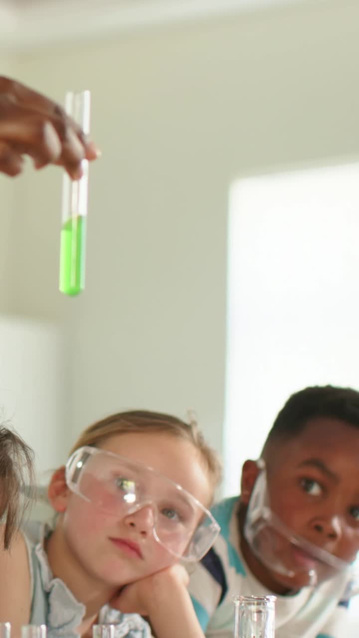 Vertical video: Watching lab teacher lifting test tube boy leaning with goggles seeing neon fluid