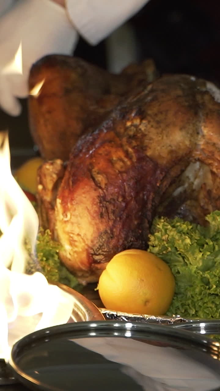 chef is cutting the baked chicken with a knife and putting the slices on the plates near the fire in the street on the summer terrace of the cafe Vertical video