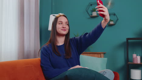 mujer en el sofá en casa con teléfono inteligente tomando selfies en cámara de teléfono móvil, llamada de video virtual en línea