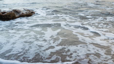 las olas vienen sobre la arena de la playa pasando las rocas y luego retroceden para volver a venir