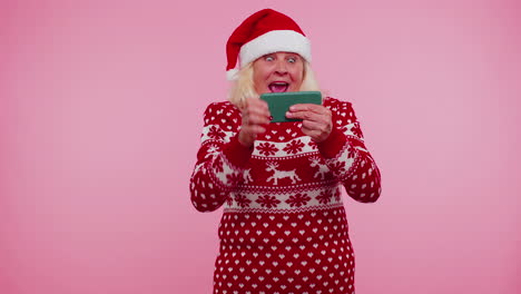 Besorgte-Großmutter-Im-Weihnachtspullover-Spielt-Begeistert-Rennvideospiele-Auf-Dem-Handy