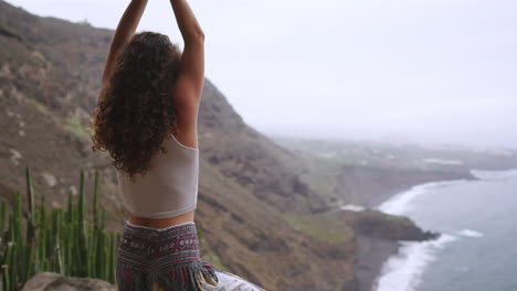 In-slow-motion,-woman-embraces-yoga's-warrior-pose-by-ocean,-beach,-and-rocky-mountains,-capturing-motivation,-inspiration,-and-connection-between-fitness-and-nature-in-healthy-living