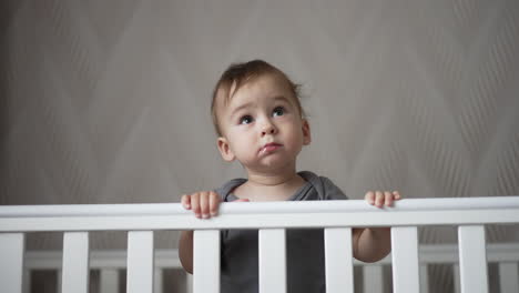 charming beautiful baby boy standing in his crib. lovely caucasian child smiling adorably showing two lower teeth.