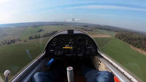 being towed in a sailplane flying above rural landscape, pilot's point of view from a cockpit