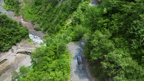 view from an above of a nissan xterra driving on steep and narrow mountain road with lush foliage in tusheti, georgia