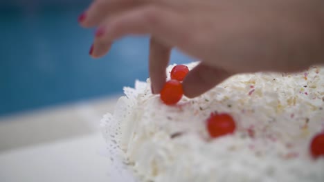 hand finishing sweet cream cake with red candy cherries on celebration event outdoors with swimming pool in the background