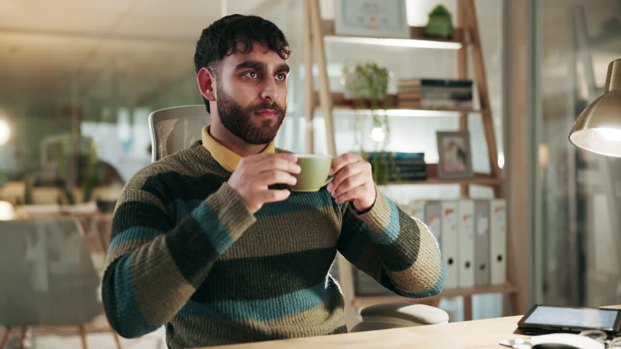 un hombre sentado en su escritorio en una oficina, sosteniendo una taza de café y mirando pensativo.