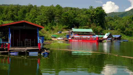 shot taken from distance of a car getting on a red barge surrounded by houseboats in pak nai fisherman village, nan province, thailand on a sunny day