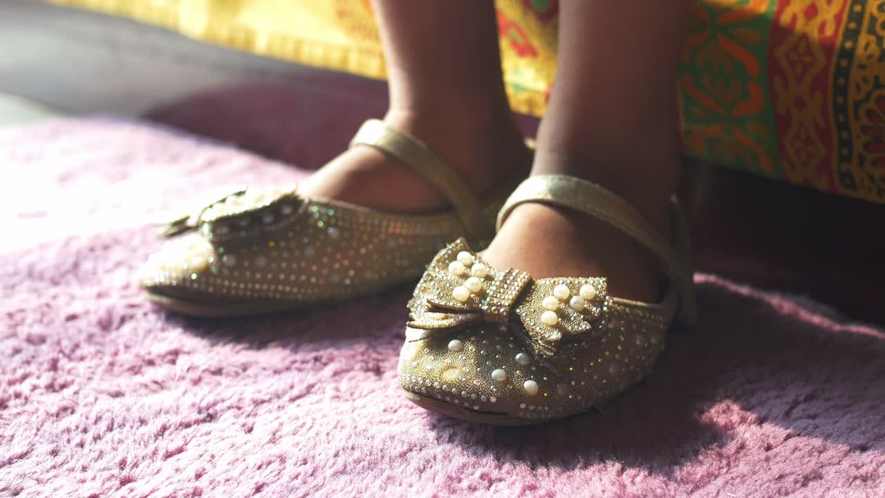 zapatos decorados con oro de la niña en una alfombra rosa